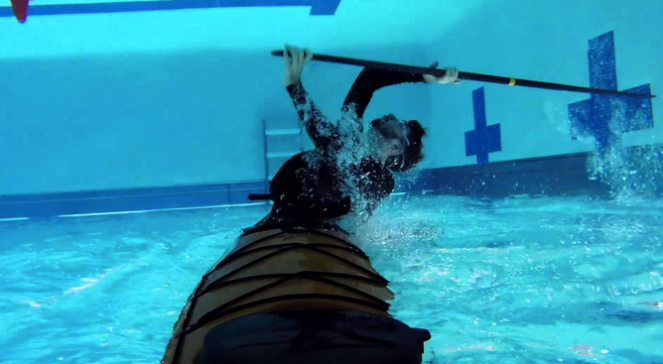 person in a sea kayak underwater in a pool, sweeping a paddle to come back up