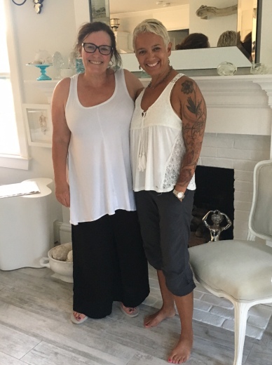 Kathy (left) and Tracy (right) in Nantucket, August 2017. Photo description: two women both in white sleeveless tops, Kathy in wide black pants, Tracy in grey capris. White fireplace mantel in background.