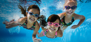 three children under water swimming, smiling.
