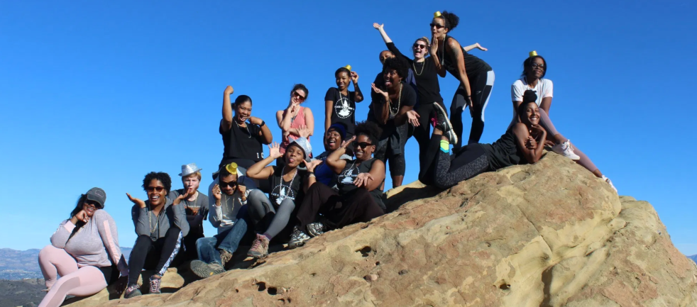 Lots of happy women of color at the top of a mountain, from Black Girls trekkin'.