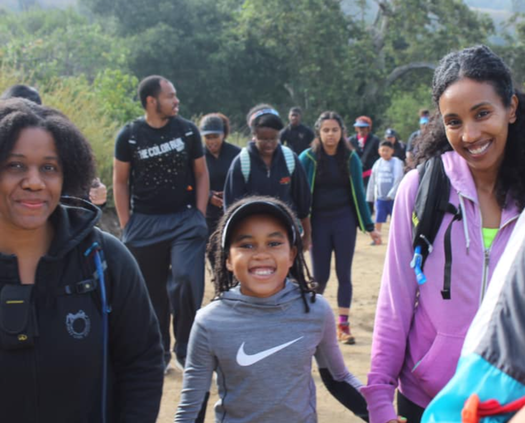 Two black women with a little girl in the middle, hiking with a big group.