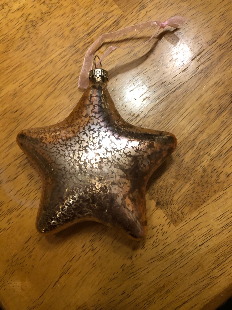 A gold star ornament   on a wooden tabletop.