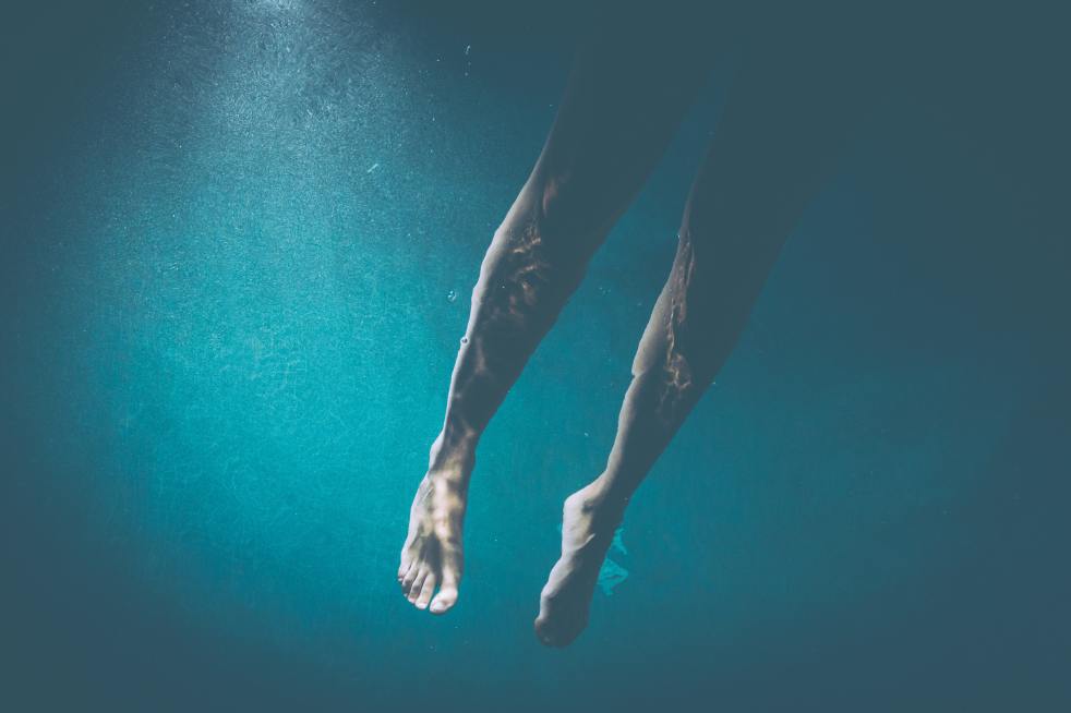 An Underwater photo of a person's legs in blue water.