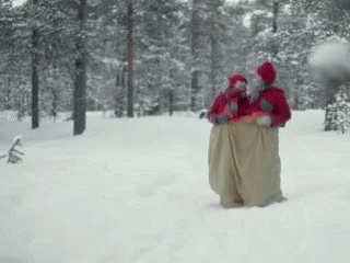 GIF of two people in red outfits hopping through the snow in a giant sack.
