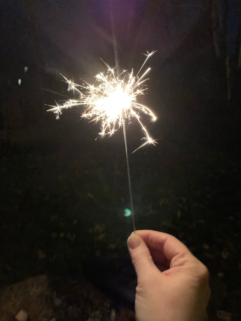 A hand holding a sparkler at night.