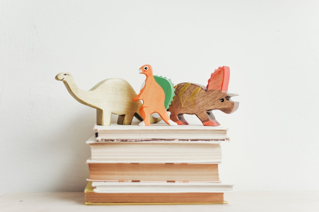 Image description: three wooden dinosaurs standing on a stack of books.​