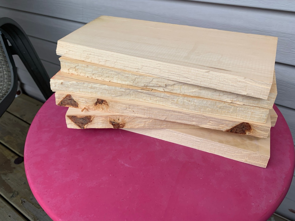 Image description: a stack of pieces of pine board that have been broken in two by my kicks and punches. The stack is sitting on a red table outdoors.