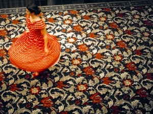 Woman in red dress twirling alone on a coloured rug